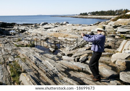 woman taking pictures of rugged rocks near ocean