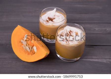 Two glasses of pumpkin latte with sliced pumpkin on a dark background. Autumn drink