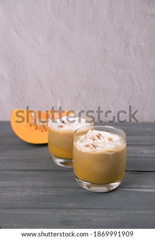 Two glasses of pumpkin latte with cream and cinnamon and a piece of sliced pumpkin on a wooden background. Vertical orientation, Copy space