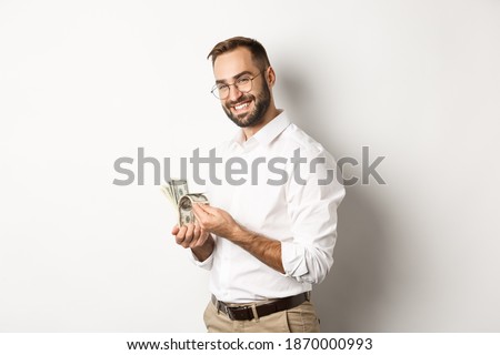 Successful business man counting money and smiling, standing against white background and looking satisfied Royalty-Free Stock Photo #1870000993