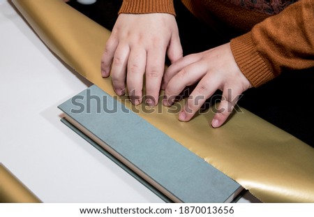 Young girl wraps book in golden color wrapping paper on table with black background