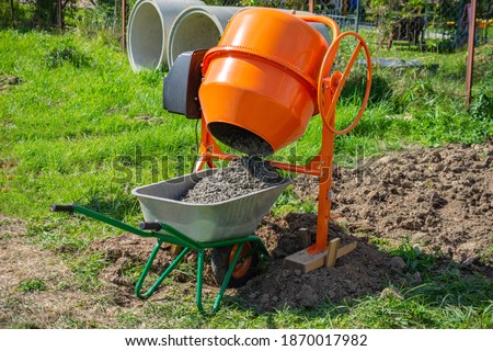 concrete is loaded into a cart from a 200 liter orange electric concrete mixer, photo taken on a sunny summer day outdoors Royalty-Free Stock Photo #1870017982