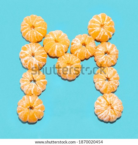 Creative layout of the letter M from peeled tangerines on a blue background. Flatlay.