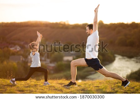 Father and cute daughter doing yoga outside in bright sunny day, lovely emotions. together at park. Family stretching after sport. Sport healthcare together. Healthy habits Royalty-Free Stock Photo #1870030300