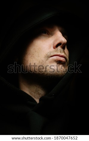 Man in a dark room in a hood like an assassin. Grain and noise artistic effect.