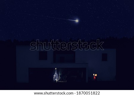 child outside in the backyard holding a sparkler making a wish while looking to a comet in a starry xmas night sky. Christmas tree lights illuminate partially the house