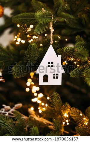 Vertical atmospheric photo Christmas decoration with a house figure on a Christmas tree with lights and balls. White House. Purchase of real estate, housing.