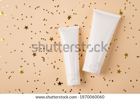 Flat lay top above close up view photo of two bottles with cream with empty clear label lying on pastel color background with golden glowing shimmer