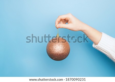 Single large golden  New Year ball for the Christmas tree in hand in light blue background: space for text, holiday banner