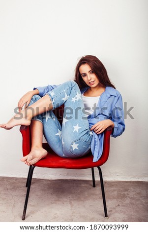 young pretty teenage hipster girl posing emotional happy smiling on white background sitting in red chair, lifestyle people concept