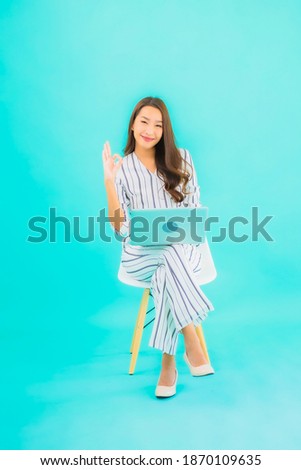 Portrait beautiful young asian woman use computer laptop and sit on chair with blue isolated background
