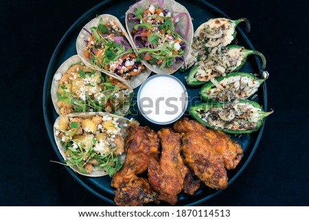 Overhead view of delicious appetizer sampler plate with chicken and steak tacos, poppers, and buffalo wings makes the mouth water and the stomach growl.