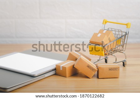 Brown paper boxs in shopping cart with laptop on wood table in office background.Easy shopping with finger tips for consumers.Online shopping and delivery service concept.