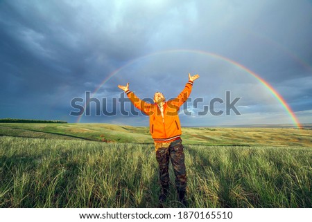 elderly man tourist raised his hands up and rejoice at the big rainbow over the steppe Spring day