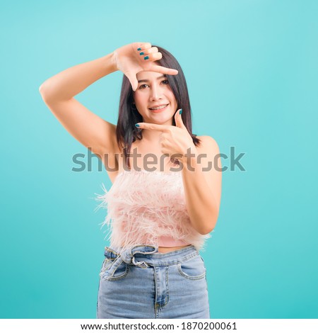 Smiling face asian beautiful woman her showing frame finger sign looking to camera on blue background, with copy space for text