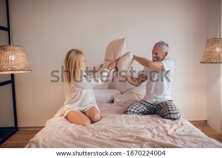 Pillow fight. Married couple having fun in bedroom and fighing with pillows