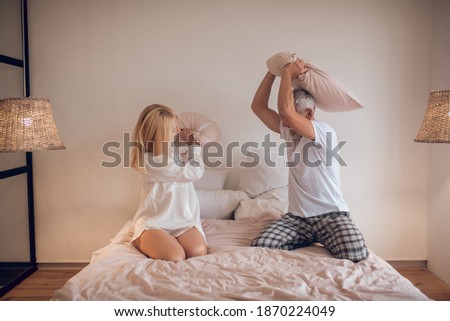 Pillow fight. Married couple having fun in bedroom and fighing with pillows