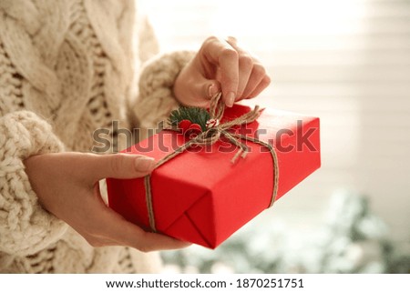 Woman holding red Christmas gift box indoors, closeup
