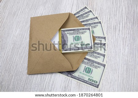 A gray envelope with a bundle of 100 dollar bills lies on a light table.