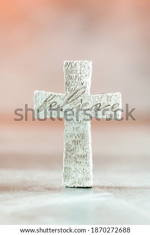 Stone cross with inscription Believe on grey background, Copy space. Christian backdrop. Biblical faith, gospel, salvation concept.