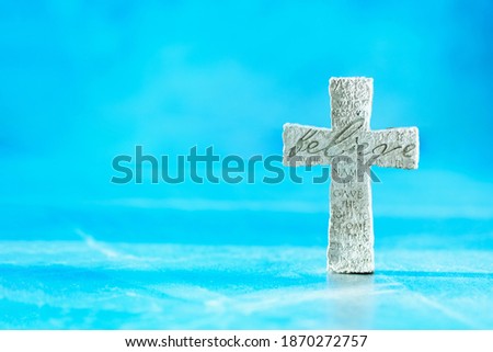 Stone cross with inscription Believe on blue background, Copy space. Christian backdrop. Biblical faith, gospel, salvation concept. Banner.