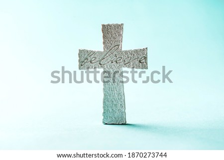 Stone cross with inscription Believe on blue background, Copy space. Christian backdrop. Biblical faith, gospel, salvation concept.