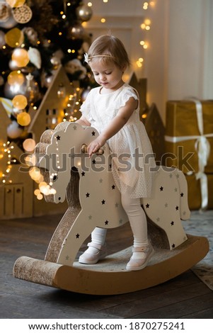 Merry Christmas and happy New year! Portrait of a little one-year-old girl on a toy horse in the living room. Concept of children's holidays and family.