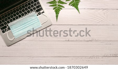 Wood office desk table with laptop, face mask and green plants. Copy space.