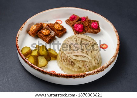 Beef tongue on a white plate, meat-in-jelly with bread with sauces and pickles. Over black background.