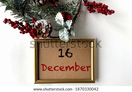 December 16 on craft paper in a gold frame.Nearby fir branches, cones and red berries on a white background.The first month of winter.Calendar for December.