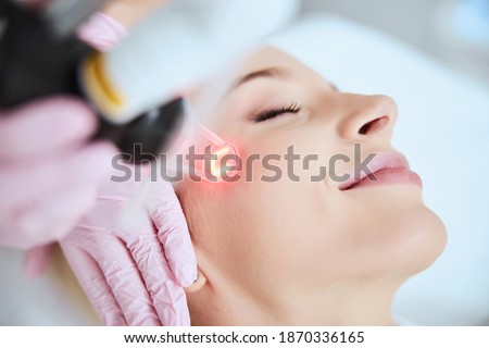 Close up portrait of a young woman patient receiving a laser treatment in a spa salon Royalty-Free Stock Photo #1870336165