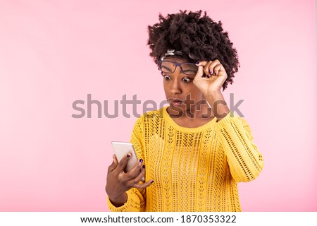 African american looking in the mobile phone, having surprised face expression. Young woman holding eyeglasses on top of a head while looking in the smartphone