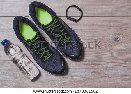 horizontal top view of a pair of black and green sport shoes, plastic bottle of water and smart wristwatch on wooden floor with copy space on the right Royalty-Free Stock Photo #1870361602