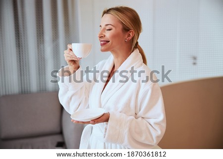 Beautiful pleased young Caucasian woman inhaling the aroma of freshly brewed herbal tea in her hand
