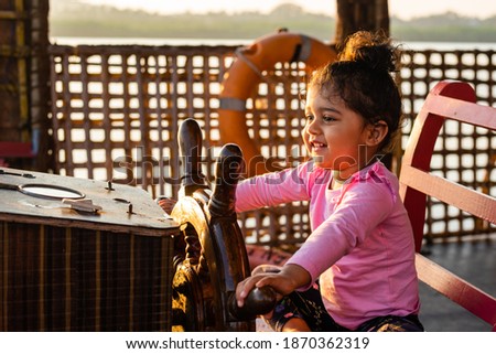 Playful Pretty Indian girl child,infant,toddler, sitting at the helm of a ship and giving joyful expressions. Dreams and vision for future of kids.