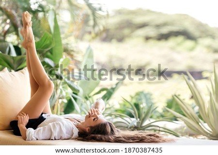 Home lifestyle woman relaxing enjoying luxury sofa on outdoor patio living room. Young female sitting on green garden terrace