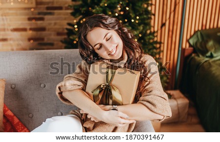 Beautiful cheerful happy young girl with christmas gifts on sofa on the background of a new year tree at home