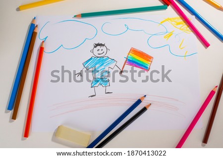 Kid's drawing of a happy boy with a rainbow flag. Color pencils, eraser and paper sheet. LGBT concept.