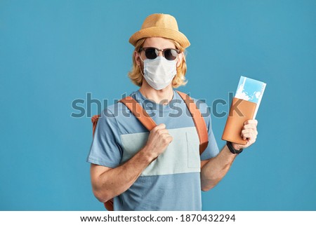 Portrait of young man in sunglasses and in mask holding tickets travelling during pandemic