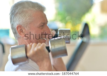 Elderly man in a gym exercising with dumbbells