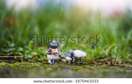 Cute plastic sheep toy standing in green grass after rain, Two Little lamb toy with blurry bokeh natural green meadow. 