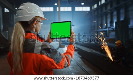 Professional Heavy Industry Engineer Uses Tablet Computer with Green Screen Mock Up Display. Female Industrial Specialist Working in a Metal Manufacture Warehouse with Sparks in the Background.