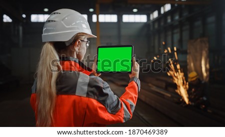Professional Heavy Industry Engineer Uses Tablet Computer with Green Screen Mock Up Display. Female Industrial Specialist Working in a Metal Manufacture Warehouse with Sparks in the Background.