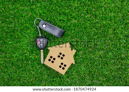 A car key with small wooden toy house on green grass.