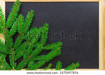Black chalk board in a wooden frame and a branch of a Christmas tree in the corner. New year and winter holidays concept. Place for text, copy space. 