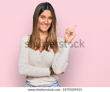 Young woman wearing casual clothes with a big smile on face, pointing with hand and finger to the side looking at the camera. 