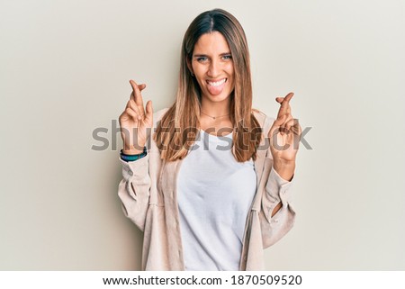 Brunette young woman doing fingers crossed gesture sticking tongue out happy with funny expression. 