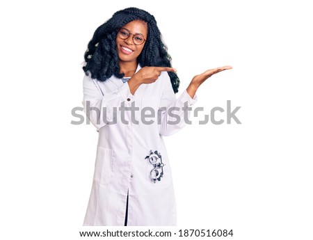 Beautiful african american optician woman with optometry glasses amazed and smiling to the camera while presenting with hand and pointing with finger. 