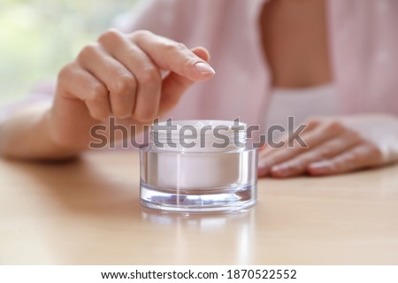 Woman with jar of moisturizing cream at table, closeup. Space for text