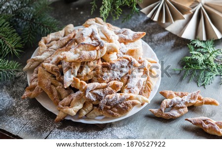 Brushwood hvorost russian traditional thin cookies with sugar powder on a white plate on wooden background with fir-tree branches. Selective focus Royalty-Free Stock Photo #1870527922